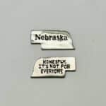 Nebraska shaped metal pocket charm with Nebraska slogan "Honestly, it's not for everyone."